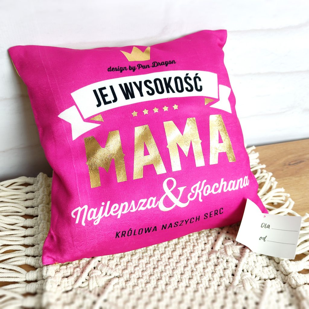 Różowa poduszka z napisem "Jej wysokość Mama najlepsza i kochana królowa naszych serc" w złotym kolorze.