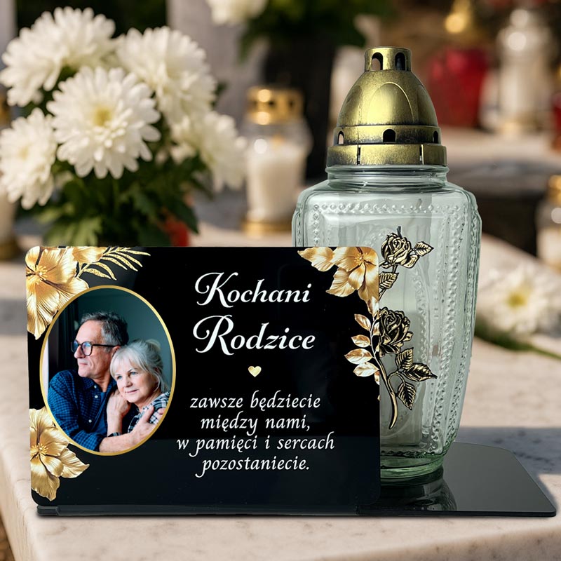 Statuetka ze Zdjęciem na Grób dla Rodziców MD1425. Personalizowana statuetka na grób z czarnej pleksi. Widoczne zdjęcie zmarłego, złote kwiaty i dedykacja, wykonane nadrukiem UV. Statuetka pełni funkcję podstawki na znicz. Pamiątka dla Mamy, Taty, Dziadka.