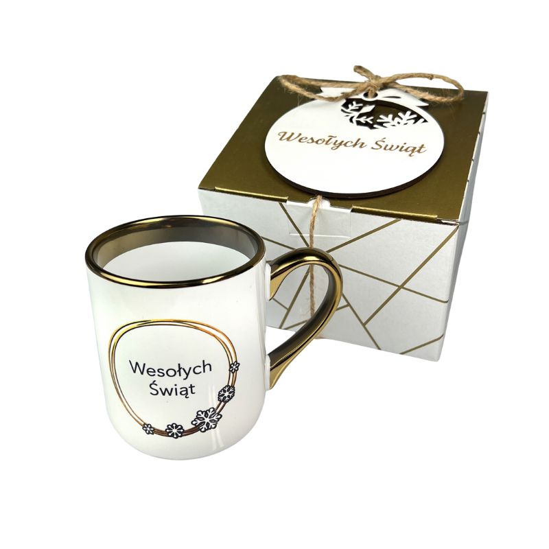 Prezent Świąteczny dla Pracowników Zestaw Kubek Świąteczny i bombka MD1650. Zestaw świąteczny z kubkiem i bombką z grawetem wesołych świąt. Kubek biały ze złotym paskiem i uchem z nadrukiem reniferka złotego.
