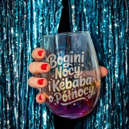 Szklanka bez nóżki z opalizującego szkła z brokatowym fioletowym dnem i napisem „Bogini Nocy i Kebaba o Północy”, obok mieniące się holograficzne pudełko z tym samym napisem i tekstem „JESTEŚ WYJĄTKOWA!”. Widok z boku na białym tle.