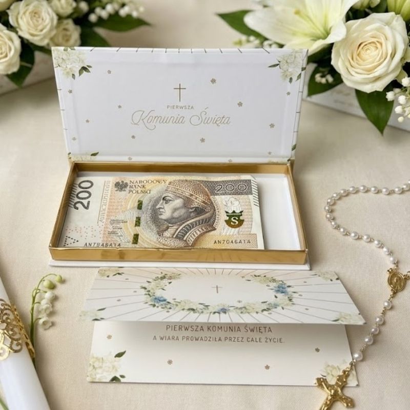 Prostokątne, eleganckie pudełko na pieniądze prezentowe na pieniądze na Pierwszą Komunię Świętą. Białe tło z delikatną złotą i zieloną grafiką roślinną oraz napisem "Pamiątka I Komunii Świętej". Pudełko jest zamknięte, widoczne pod lekkim skosem na jasnym tle.