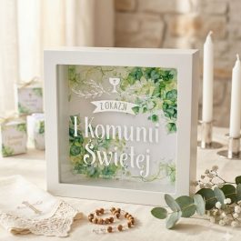 Skarbonka w formie białej ramki 15x15 cm z nadrukiem na szkle „Z okazaji I Komunii Świętej” na tle grafik zielonych liści i kielicha z hostią. Widok z perspektywy.