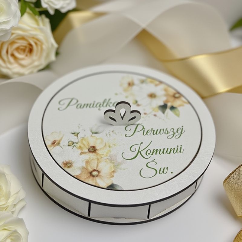 Białe okrągłe drewniane pudełko na pamiątkę Pierwszej Komunii Świętej z akwarelowym motywem żółtych kwiatów i ozdobnym napisem.