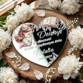 Prezenciki dla gości. Personalizowany magnes na podziękowanie komunijne w kształcie serca ze srebrnej pleksi lustrzanej, z kolorowym nadrukiem modlącej się dziewczynki w wianku, otwartą Biblią, ozdobnym nadrukiem i Polish text "Dziękuję za obecność w tym wyjątkowym dniu Natalia 17.05.2027", położony na plaster drewna i otoczony białymi peoniami i gipsówką, w jasnym świetle dziennym.