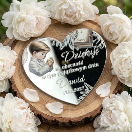 Ekskluzywne prezenty dla gości. Personalizowany magnes na podziękowanie komunijne w kształcie serca ze srebrnej pleksi lustrzanej, z kolorowym nadrukiem modlącego się chłopca, otwartą Biblią, ozdobnym nadrukiem i Polish text "Dziękuję za obecność w tym wyjątkowym dniu Natalia 17.05.2027", położony na plaster drewna i otoczony białymi peoniami i gipsówką, w jasnym świetle dziennym.