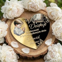 Magnes na lodówkę dla gości. Personalizowany magnes na podziękowanie komunijne w kształcie serca ze złotej pleksi lustrzanej, z kolorowym nadrukiem modlącego się chłopca, otwartą Biblią, ozdobnym nadrukiem i Polish text "Dziękuję za obecność w tym wyjątkowym dniu Natalia 17.05.2027", położony na plaster drewna i otoczony białymi peoniami i gipsówką, w jasnym świetle dziennym.