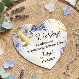 Upominek na podziękowanie dla gości. Spersonalizowany magnes komunijny w kształcie serca z białego HDF, prezentowany na naturalnym plastrze drewna w otoczeniu gałązek eukaliptusa i różańca. Na magnesie widoczny jest trwały nadruk UV: złota gołębica, kielich eucharystyczny oraz fioletowo-niebieskie kwiaty. Tekst na magnesie: "Dziękuję za obecność w tym wyjątkowym dniu, Jakub, 17.05.2027".