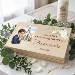 Drewniane pudełko na pieniądze z okazji Pierwszej Komunii Świętej dla chłopca. Na wieku personalizowany nadruk w stylu akwareli przedstawiający modlącego się chłopca, kościół oraz białe róże ze złotymi elementami. Widoczny napis: "Pamiątka I Komunii Świętej Pawła 24.05.2027". Produkt pokazany na białym tle w rzucie izometrycznym.
