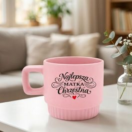 Elegancki kubek. Różowy kubek ceramiczny z ozdobnym napisem Najlepsza Matka Chrzestna, kwadratowym uchem i ryflowaną podstawą na białym tle.