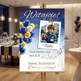 Tablica urodzinowa witacz na 18 urodziny Kuby ze zdjęciem i złotymi balonami, stojąca na drewnianej sztaludze w udekorowanej sali.